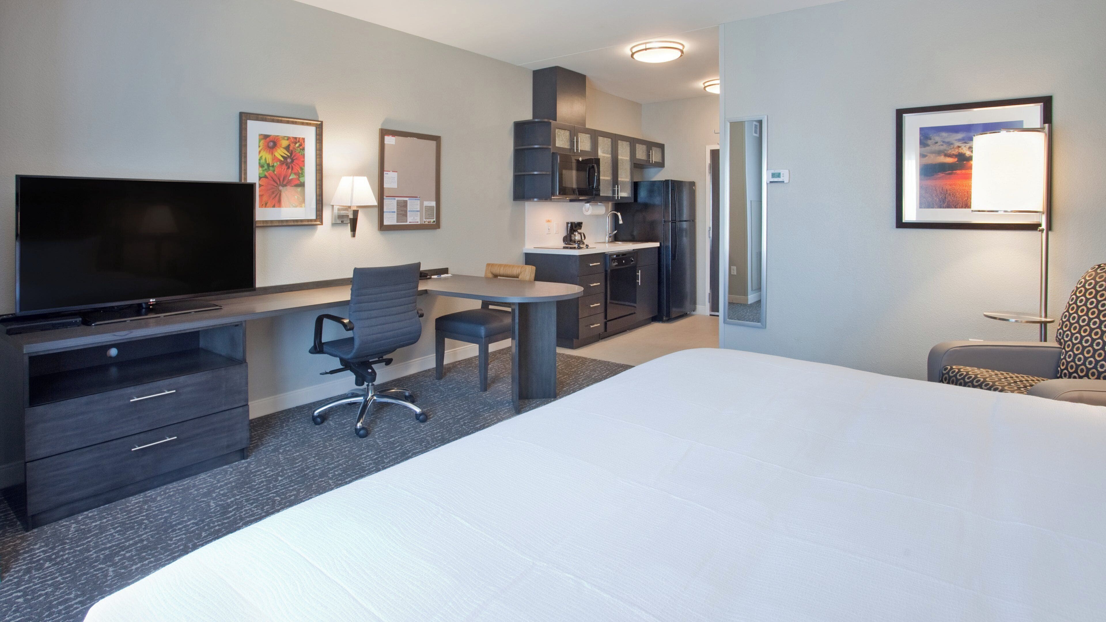 A hotel room with a bed, a desk with a chair, a television, a kitchenette, and a bathroom.