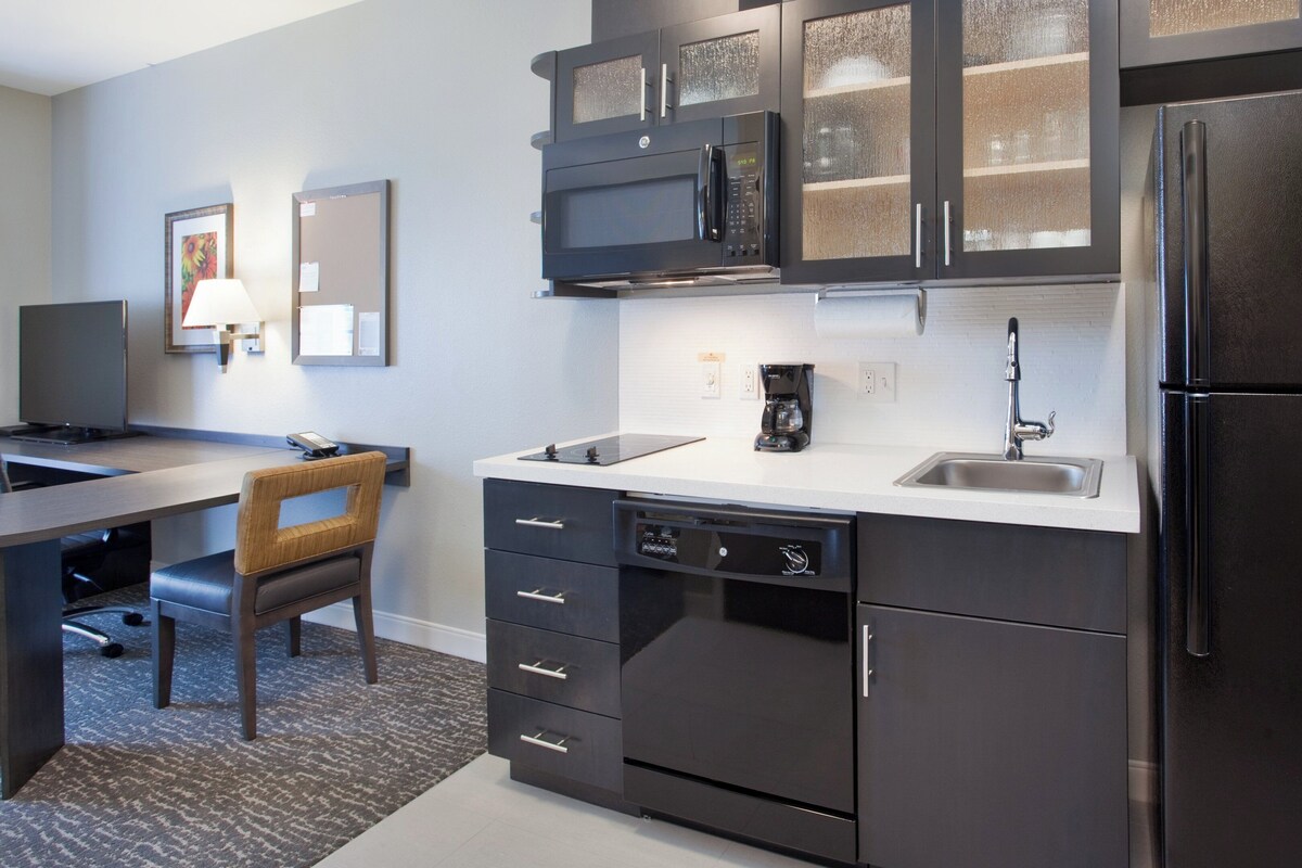 A modern kitchen with black cabinetry, a built-in microwave, and a coffee maker.