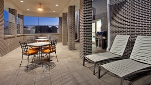 Une terrasse extérieure avec des murs en briques, un barbecue et des espaces aménagés pour s’asseoir.