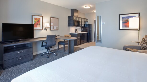 Une chambre d’hôtel dotée d’un grand lit, d’un bureau avec une chaise, d’une télévision, d’une kitchenette et d’œuvres d’art accrochées aux murs.