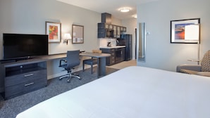 Une chambre d’hôtel dotée d’un grand lit, d’un bureau avec une chaise, d’une télévision, d’une kitchenette et d’œuvres d’art accrochées aux murs.