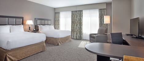 A hotel room with two beds, a desk, a chair, a TV, and a window with curtains.
