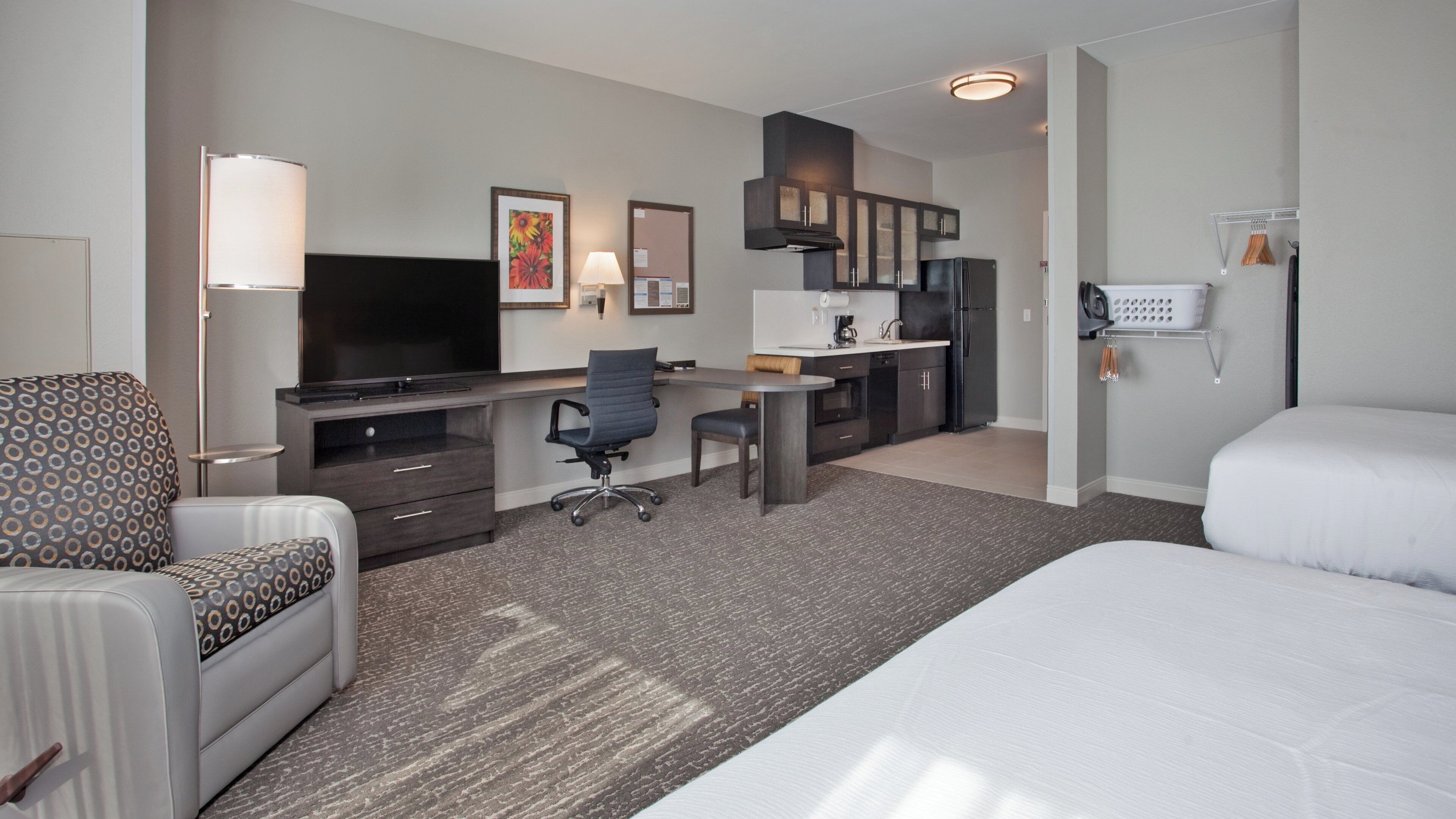 Habitación de hotel con cama, escritorio, silla, televisión, zona de cocina y baño.