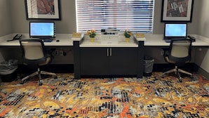 Un espacio de trabajo con dos escritorios, cada uno con una computadora, sillas y una ventana con persianas.