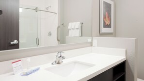 Un bany modern amb un rentapans blanc, un mirall, una dutxa i una fotografia encadrada a la paret.