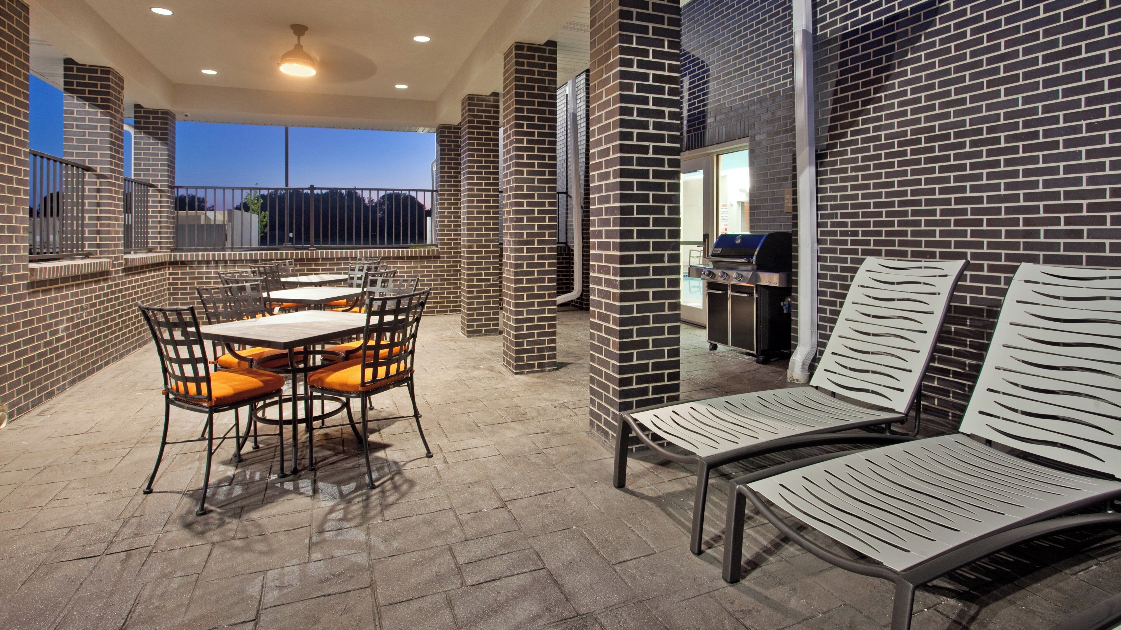 An outdoor patio with brick walls, tables, chairs, and a barbecue grill.