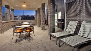 Une terrasse extérieure avec des murs en briques, des tables, des chaises et un barbecue.