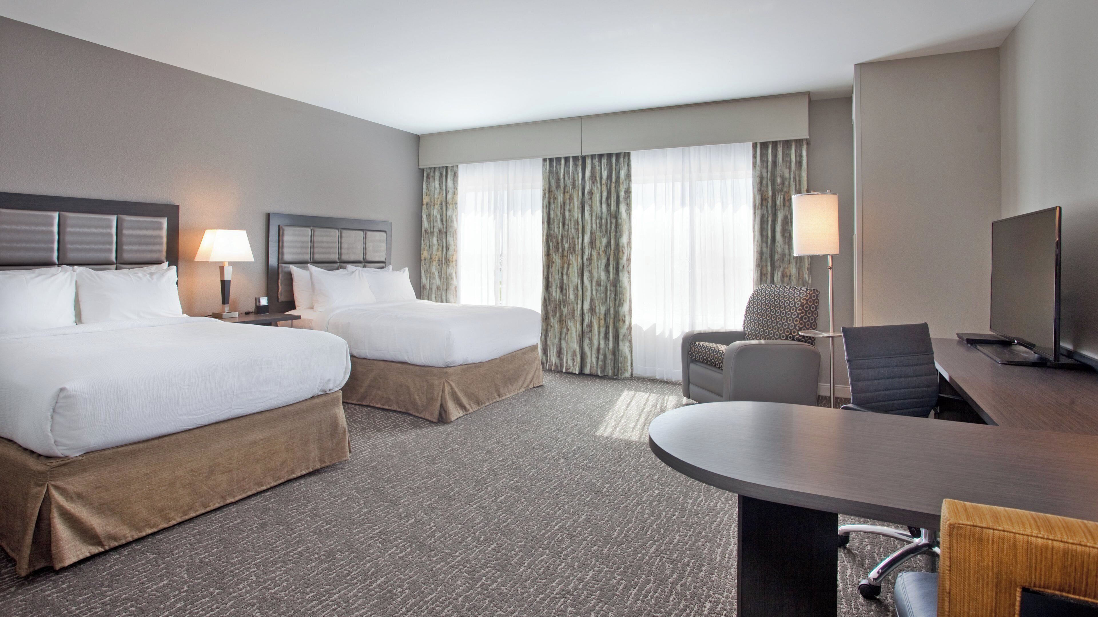 A hotel room with two beds, a desk, a chair, a TV, and a window with curtains.