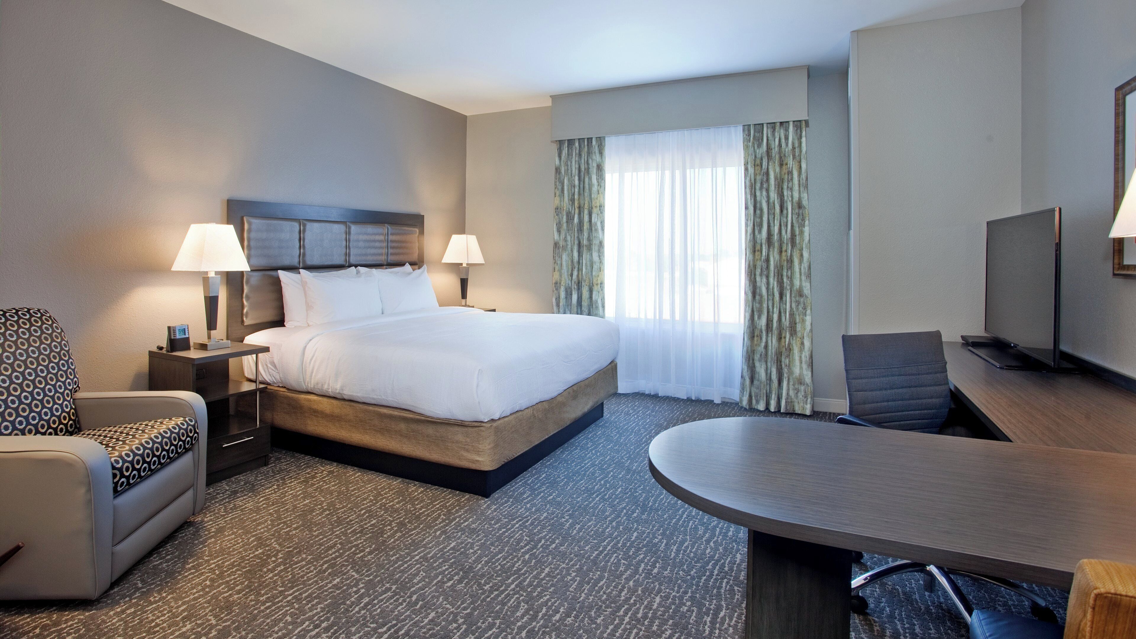 A hotel room with a large bed, two bedside lamps, a desk with a chair, and a television on a stand.