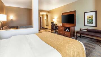 A hotel room with a large bed, a desk with a chair, a television, a bench, and a framed picture on the wall.