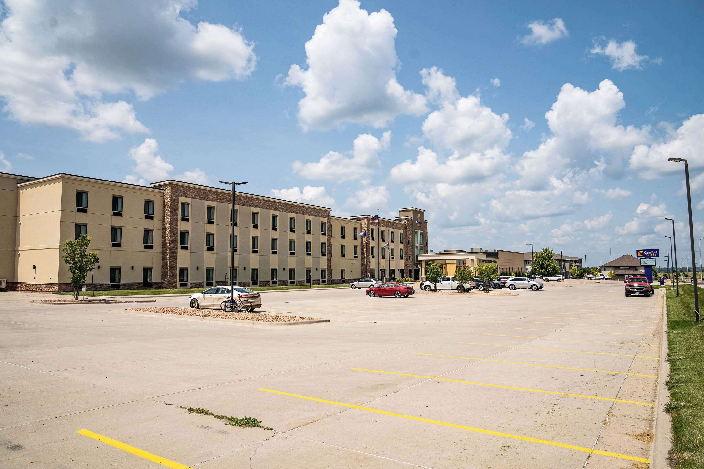 A parking lot with several cars, a building with multiple floors, and a clear sky with clouds.