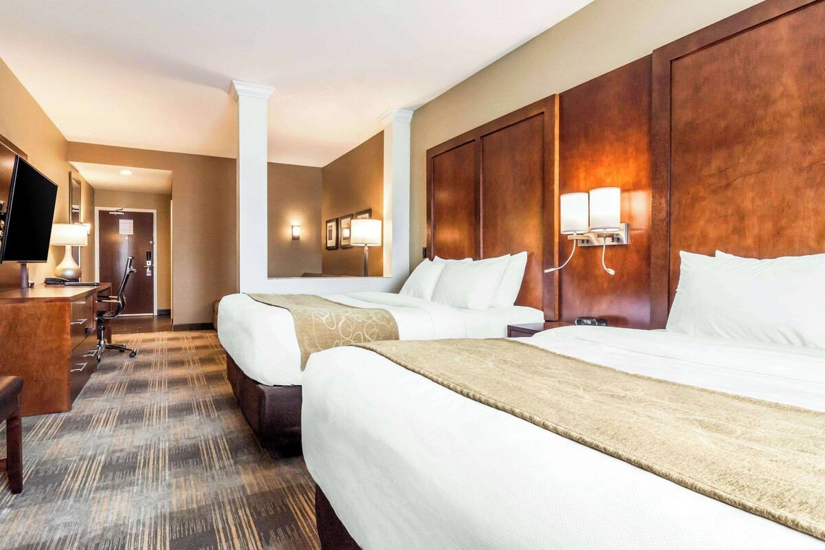 A hotel room with two beds, a desk, a chair, and a television.