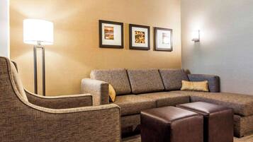 A modern living room with a sectional sofa, a single armchair, and a coffee table. There are three framed pictures on the wall and a floor lamp.