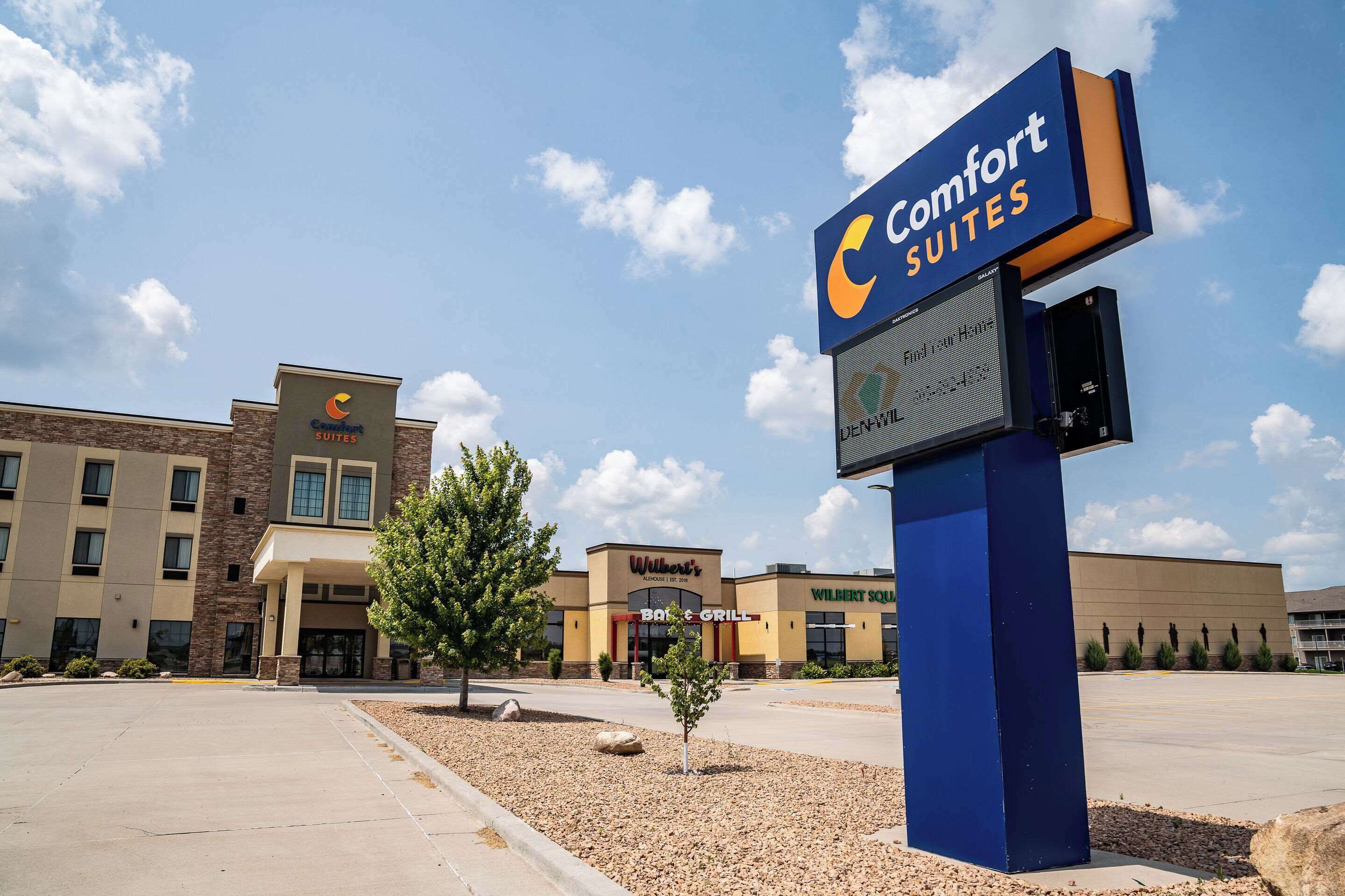 Un hotel con un letrero de Comfort Suites, un restaurante B&B Grill y un edificio Wilbert Suites.