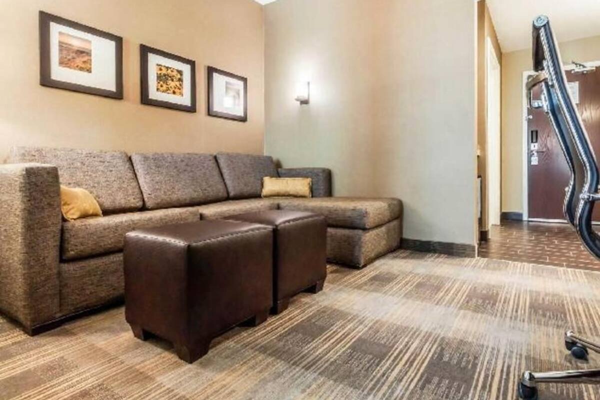 A living room with a sectional sofa, ottomans, framed pictures on the wall, and a carpeted floor.