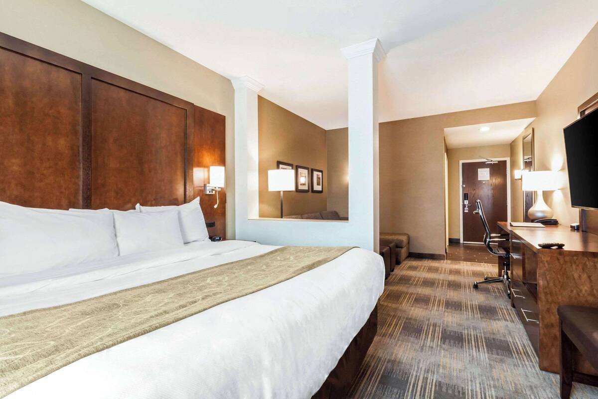 A hotel room with a large bed, a desk with a chair, a TV, and a mirror.