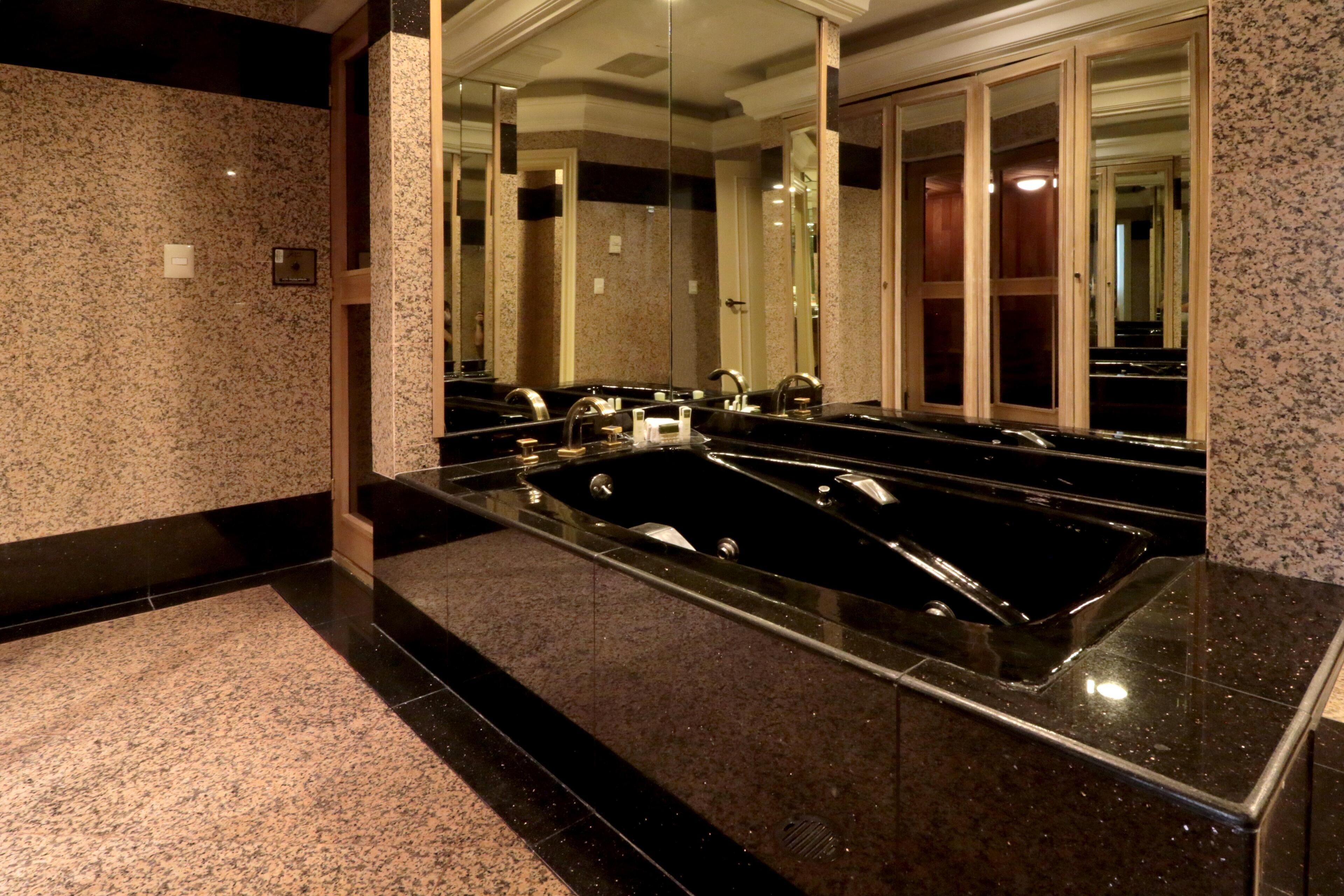 A modern bathroom with a large mirror, a black bathtub, and granite countertops.