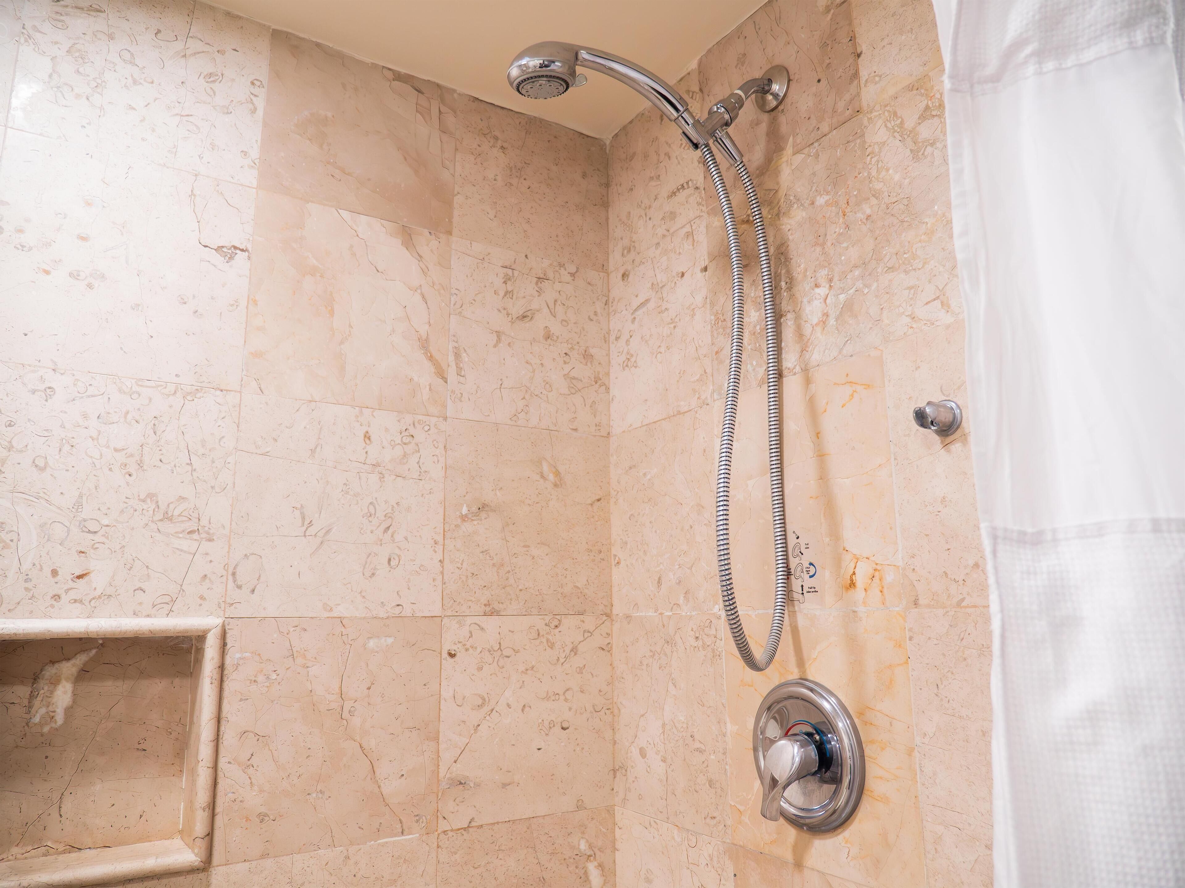 A shower with a handheld showerhead and a wall-mounted faucet.