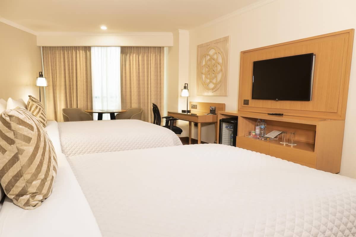 Ett hotellrum med två sängar, ett skrivbord, en tv och en minibar.