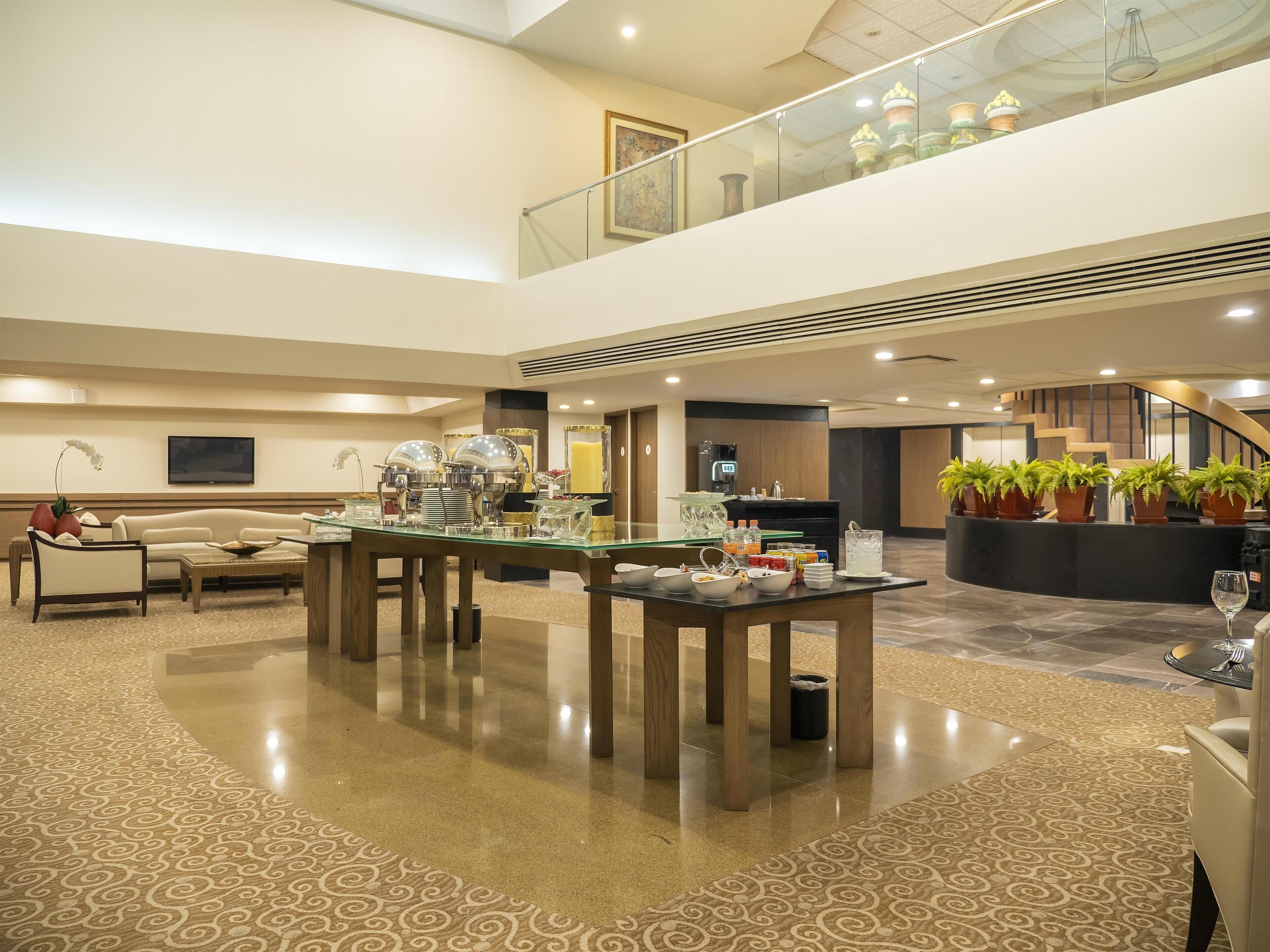 A spacious lobby with a central coffee station, seating area, and a staircase leading to an upper level.