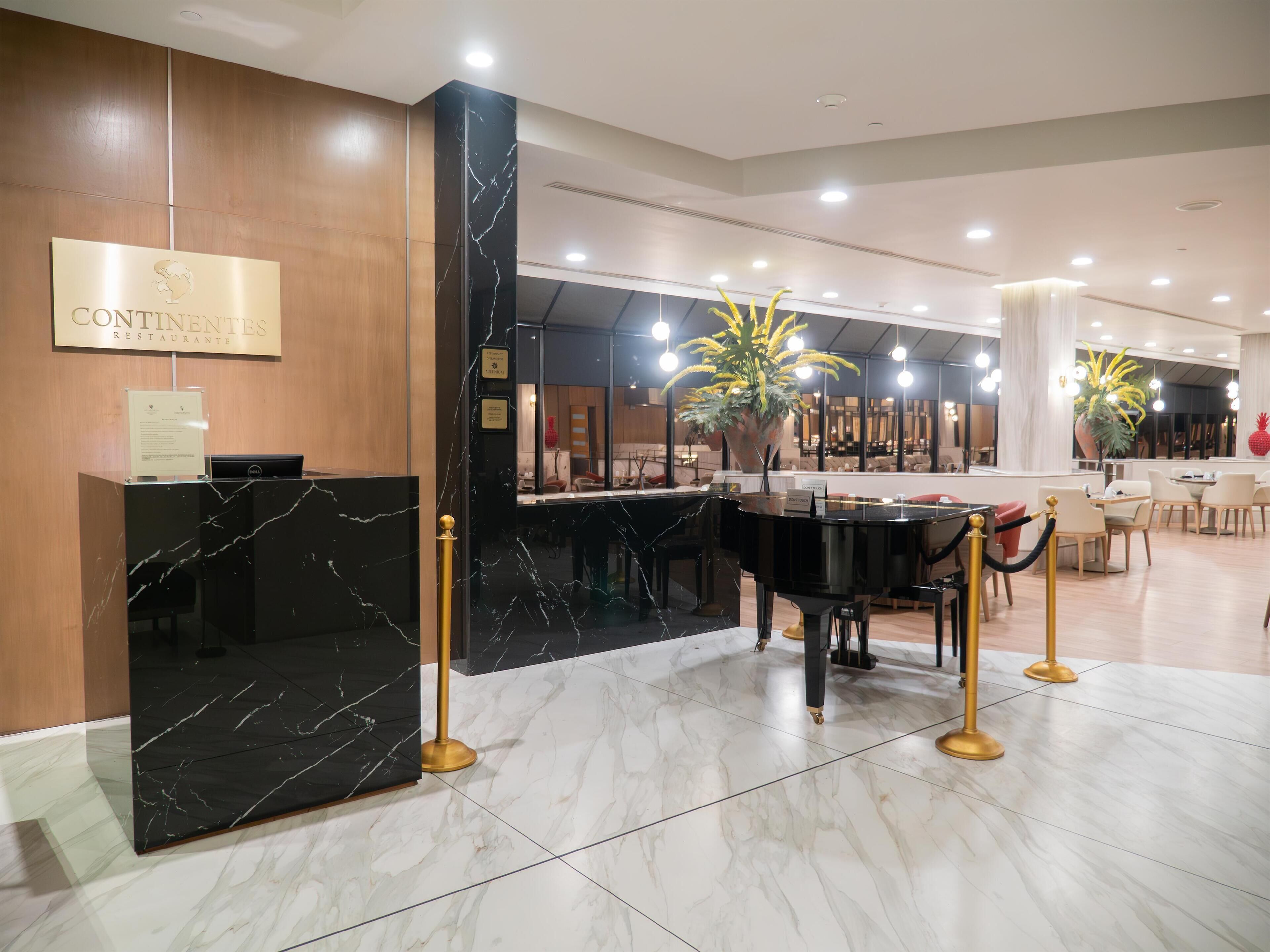 A modern restaurant interior with marble flooring, a reception desk, and a dining area with tables and chairs.