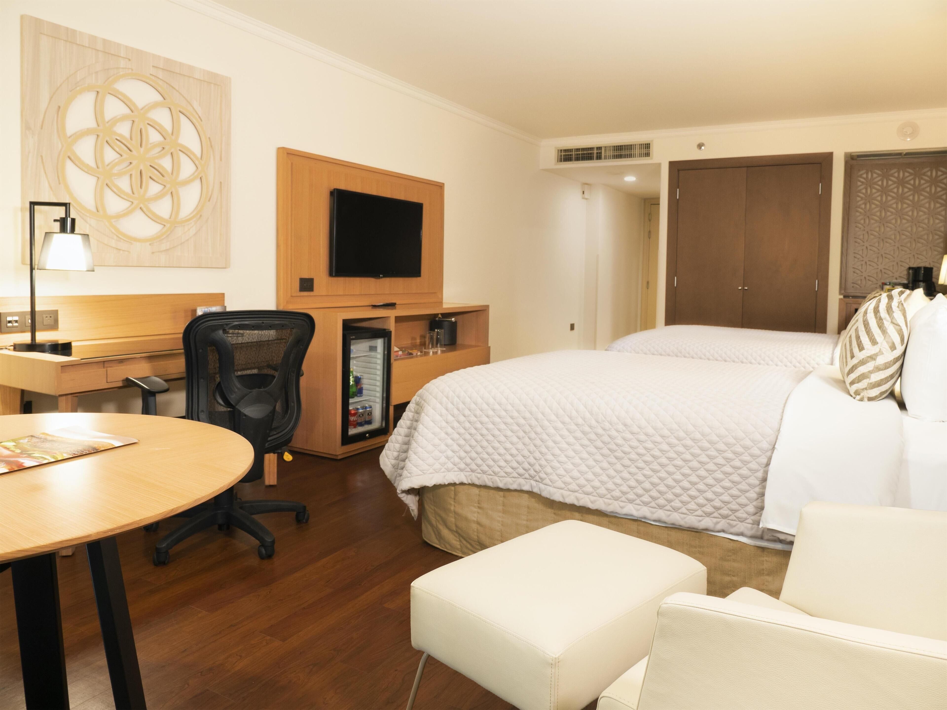 Une chambre d’hôtel comprenant un lit, un bureau avec une chaise, une télévision, un minibar et une armoire.
