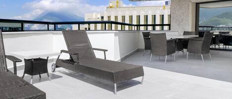 Terraço no telhado com móveis de vime, área de refeições e vista para a cidade e montanhas.