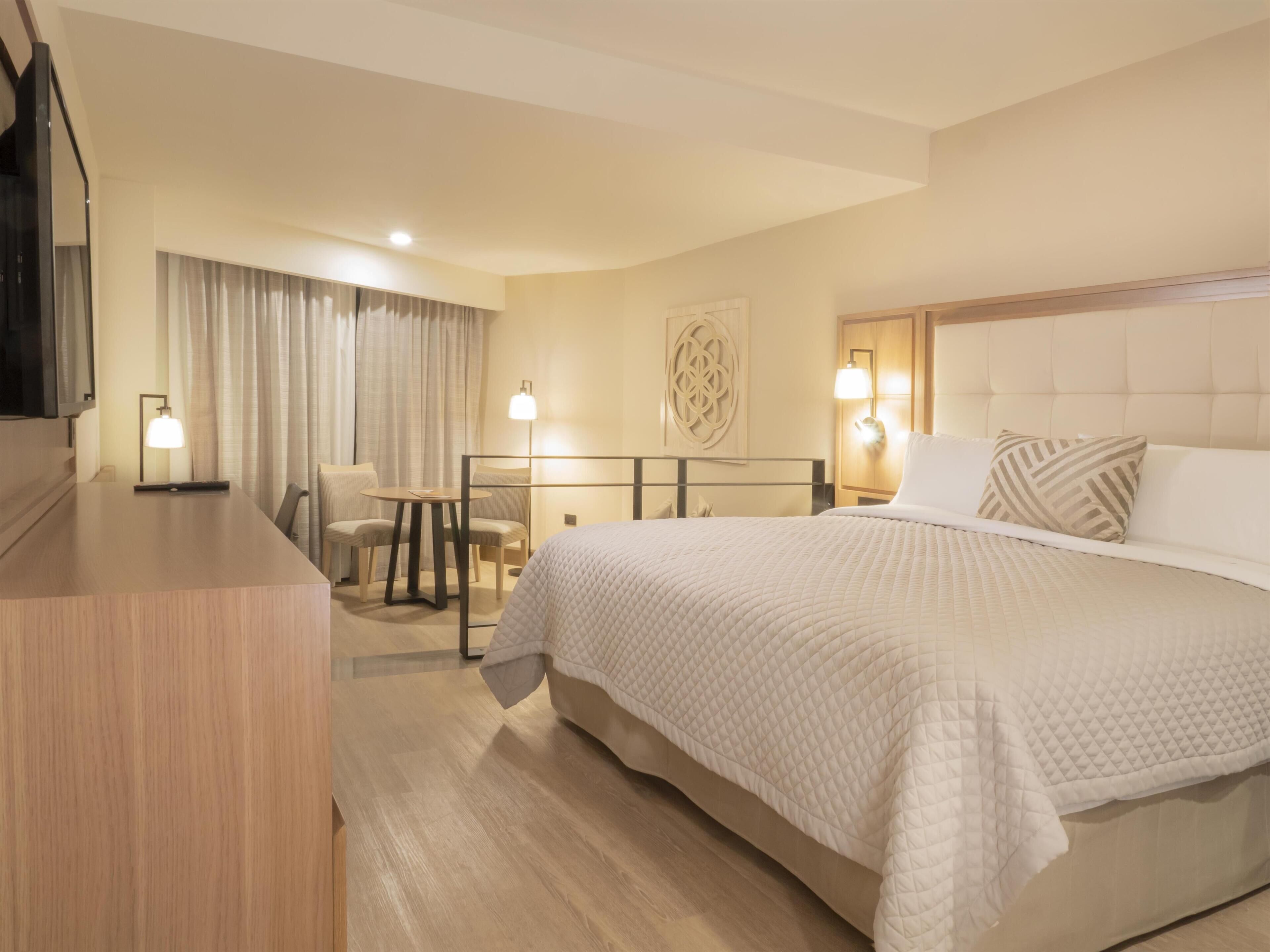 Habitación de hotel con una cama grande, un escritorio con silla, una televisión y una lámpara fijada a la pared.