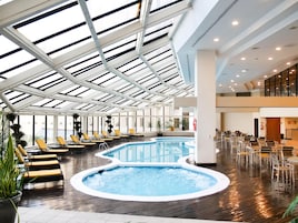 Una piscina interior amplia con techo de cristal, rodeada de sillones de descanso y un área de comedor.