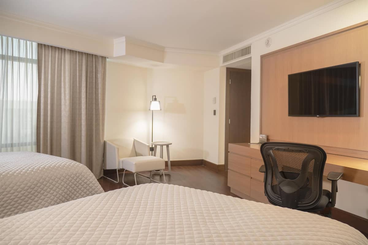 Ett hotellrum med två sängar, ett skrivbord, en stol, en tv och en lampa.