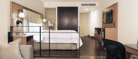 A hotel room with a bed, a desk, a chair, a sofa, a TV, and a wardrobe.