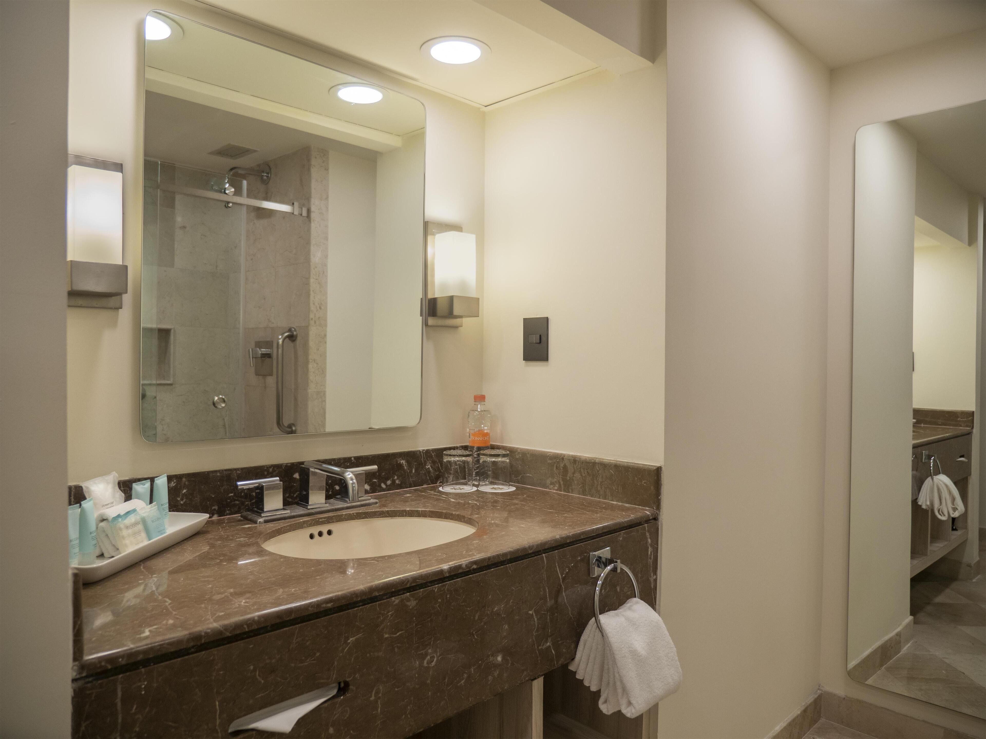 A modern bathroom with a marble sink, a large mirror, and a towel rack.