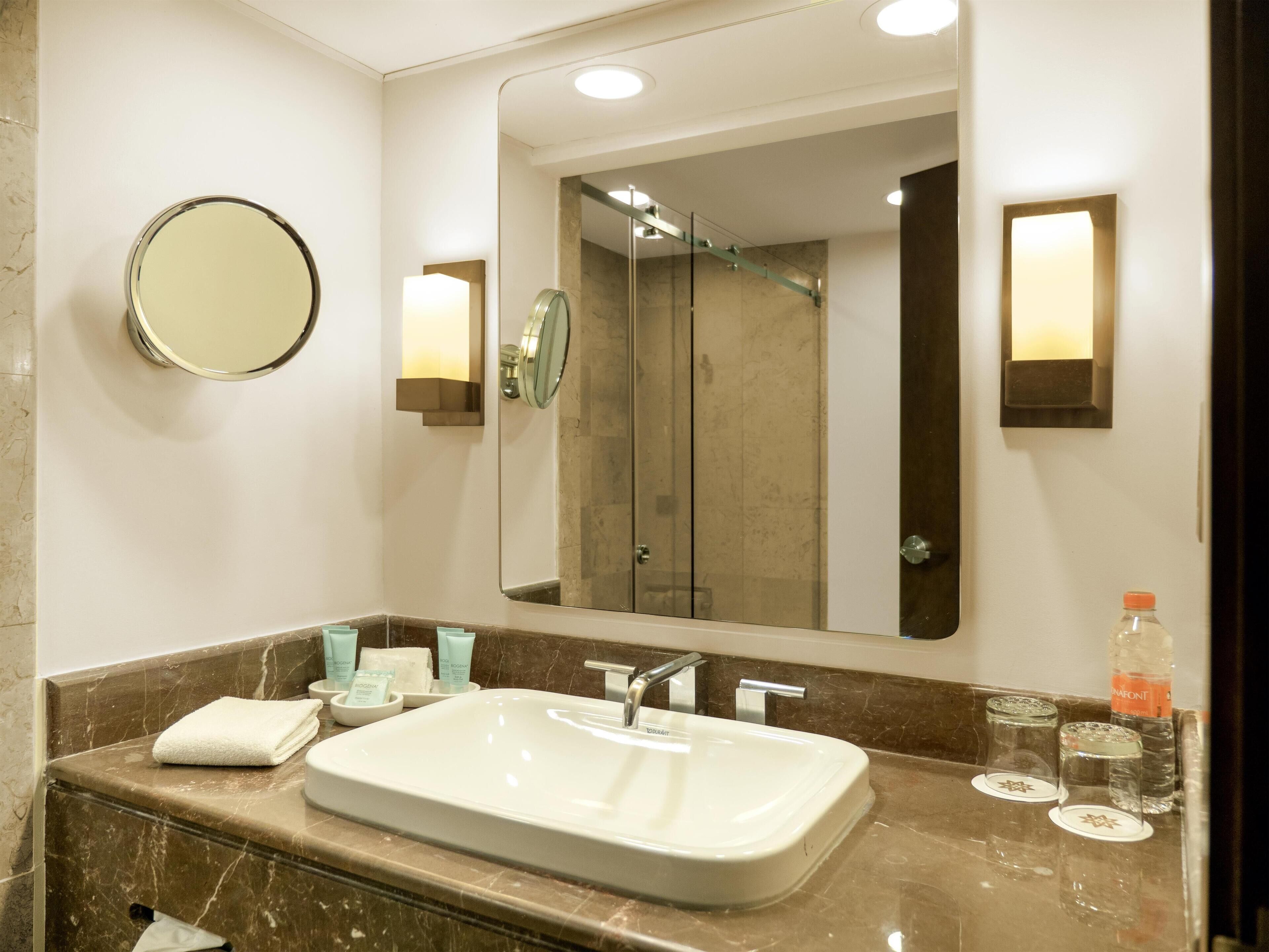Un baño moderno con un espejo grande, un lavamanos blanco y artículos de aseo en la encimera.