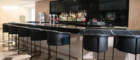 Zona de bar moderna con una barra alargada, varios taburetes y una amplia variedad de botellas y vasos.