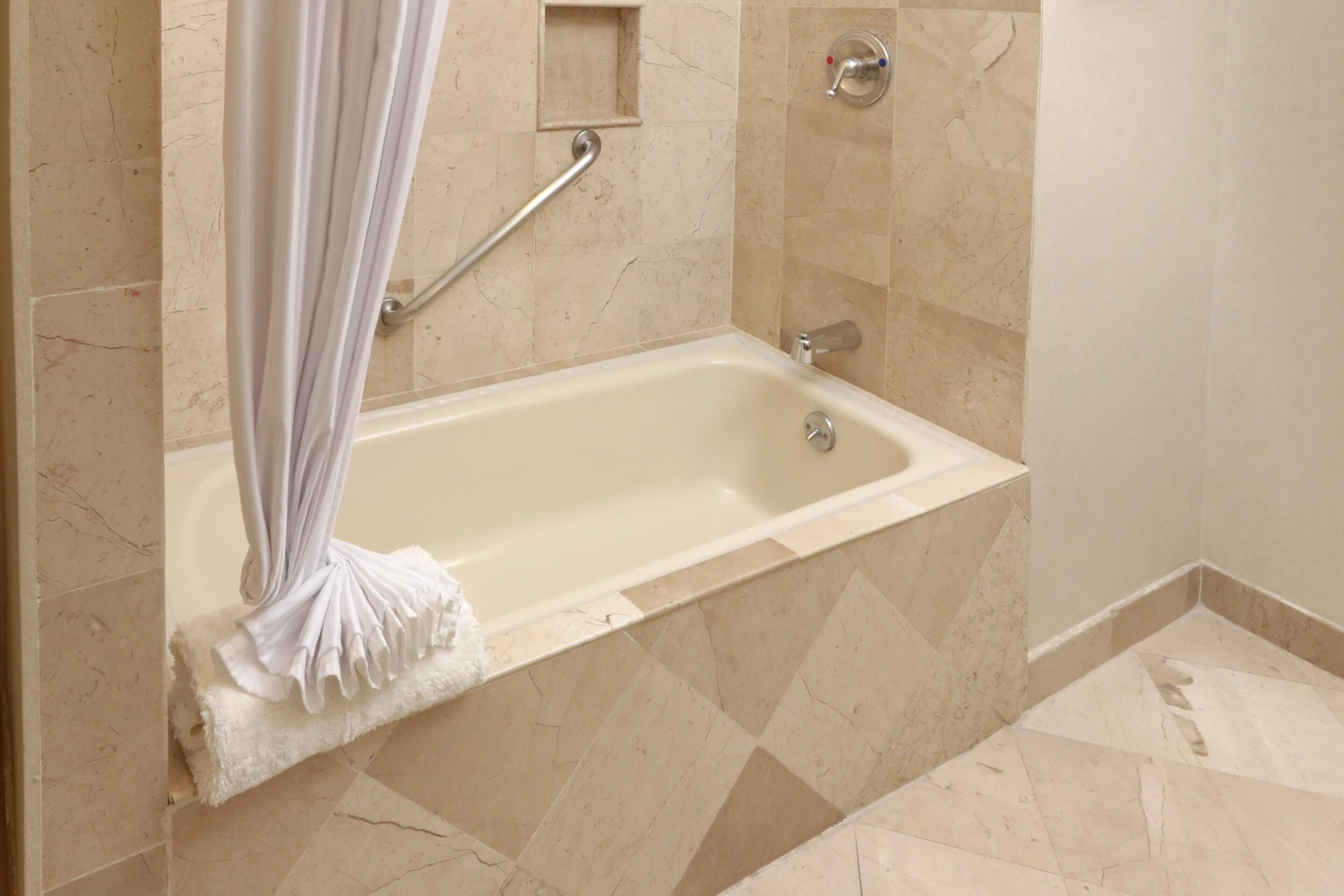 Une salle de bain équipée d’une baignoire, d’une zone de douche et d’une barre d’appui.