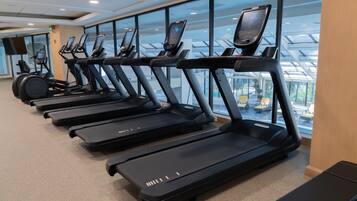 Varias cintas de correr en un gimnasio con amplias ventanas y vistas a una zona de piscina.