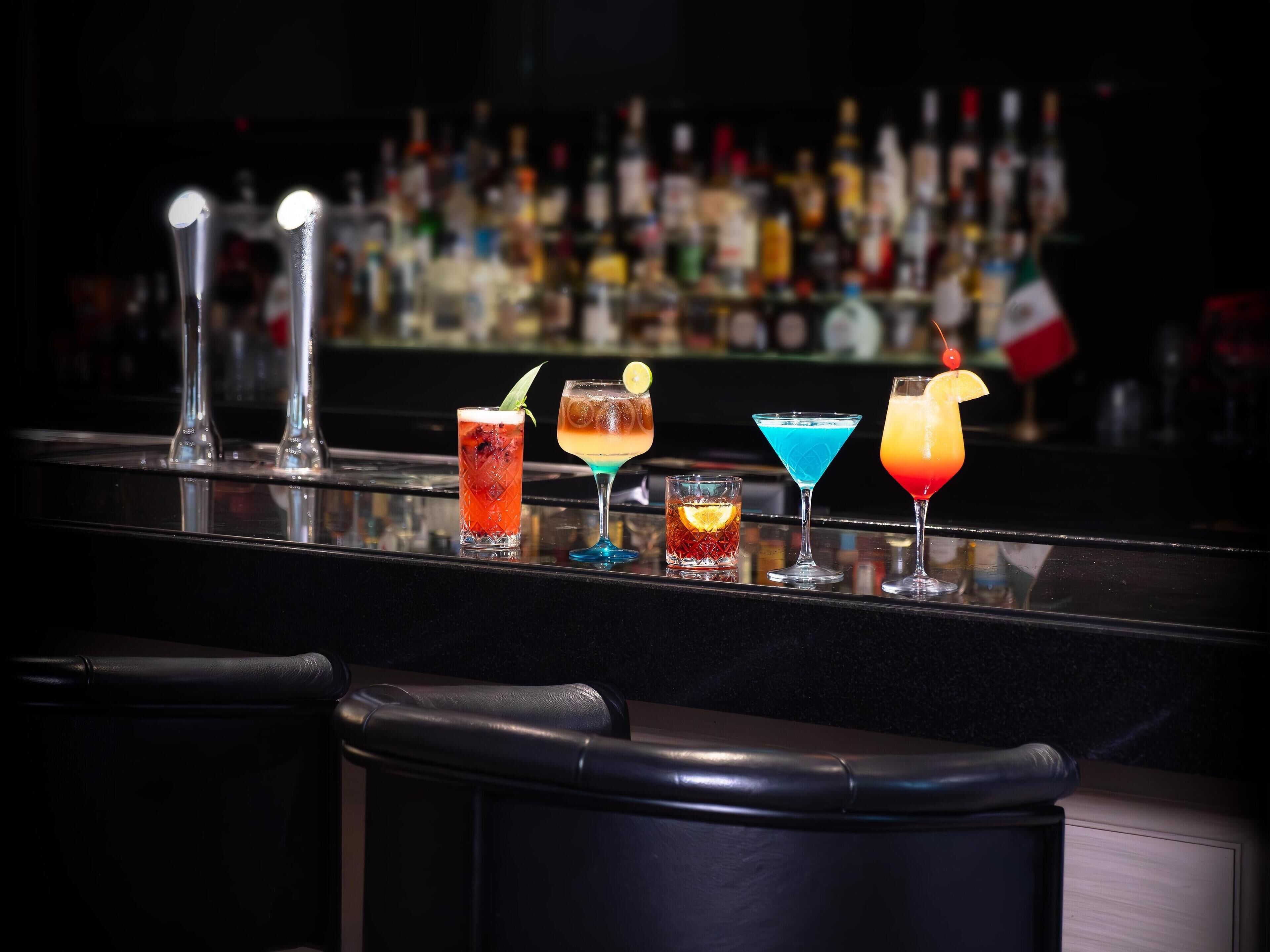 A bar counter with various cocktails and bottles in the background.