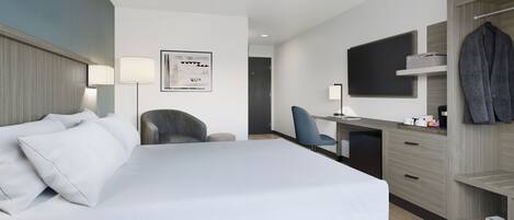 A modern hotel room with a large bed, a desk, a chair, a wardrobe, and a flat-screen TV.