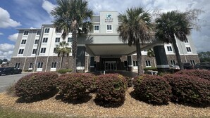 A multi-story hotel with a central entrance, palm trees, and a parking area. - Hyatt Select Valdosta (Valdosta)