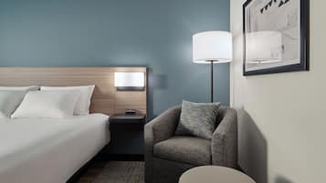 A hotel room with a bed, a nightstand, a lamp, a chair, and a rug.