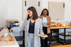 A buffet setup with a person serving food, a food display unit, and a counter with various items. - Hyatt Select Valdosta (Valdosta)