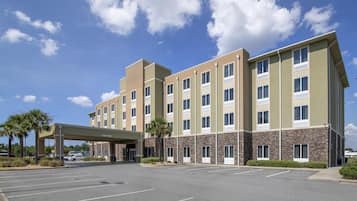 A multi-story hotel with a covered entrance, parking lot, and a clear sky.