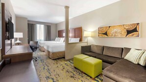 A hotel room with a bed, a sofa, a desk with a lamp, a TV, and a painting on the wall.