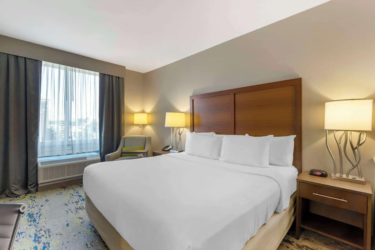 Ein Hotelzimmer mit einem großen Bett, zwei Nachttischlampen, einem Nachttisch, einem Sessel und einem Fenster mit Vorhängen.