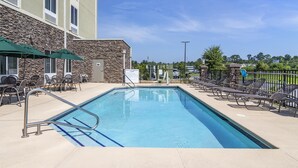 A swimming pool with lounge chairs and umbrellas, surrounded by a stone building and a fenced area with trees. - Hyatt Select Valdosta (Valdosta)