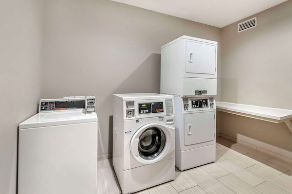 A laundry room with a front-loading washer and dryer, a tall cabinet, and a small shelf. - Hyatt Select Valdosta (Valdosta)