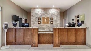 A reception area with a stone wall, two wooden counters, a mounted TV, and a digital kiosk.