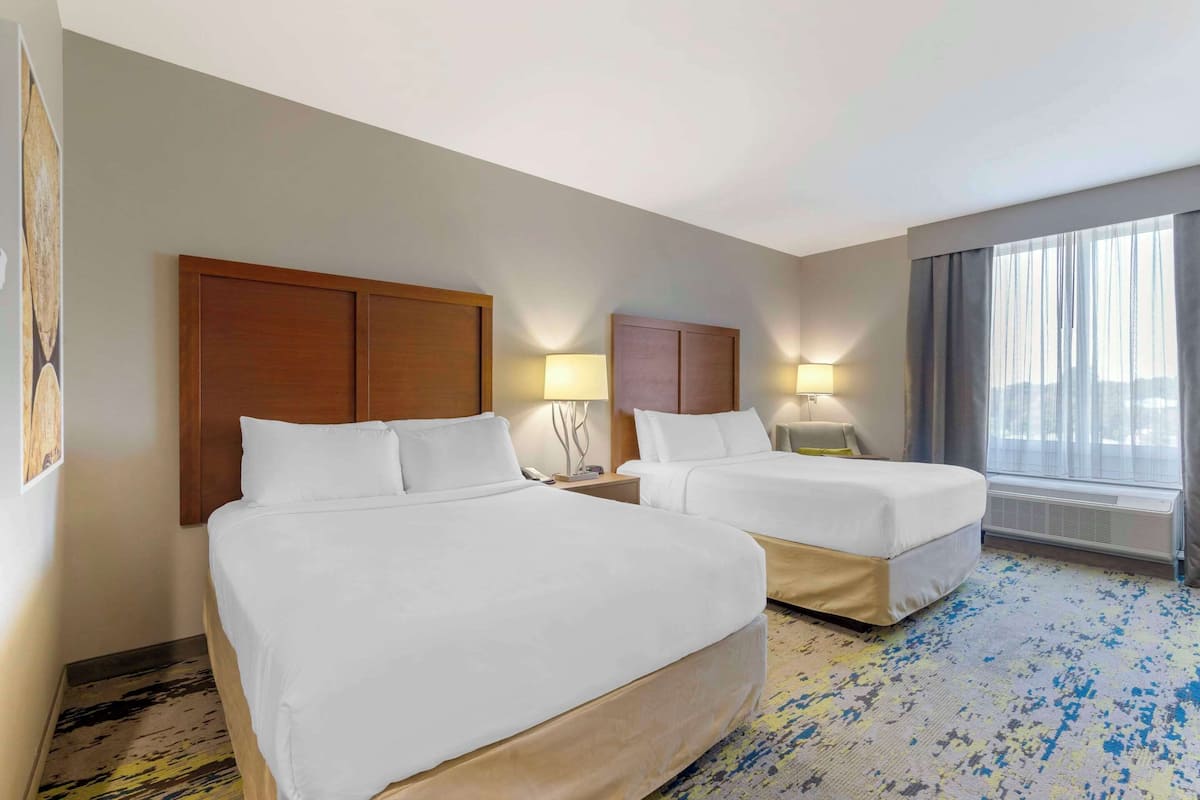 Ein Hotelzimmer mit zwei Betten, einem großen Fenster mit Vorhängen und einem Teppichboden.