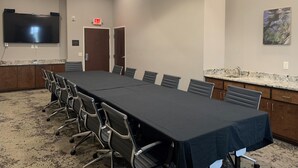 A conference room with a long table, chairs, a flat-screen TV, an exit sign, and a painting on the wall. - Hyatt Select Valdosta (Valdosta)