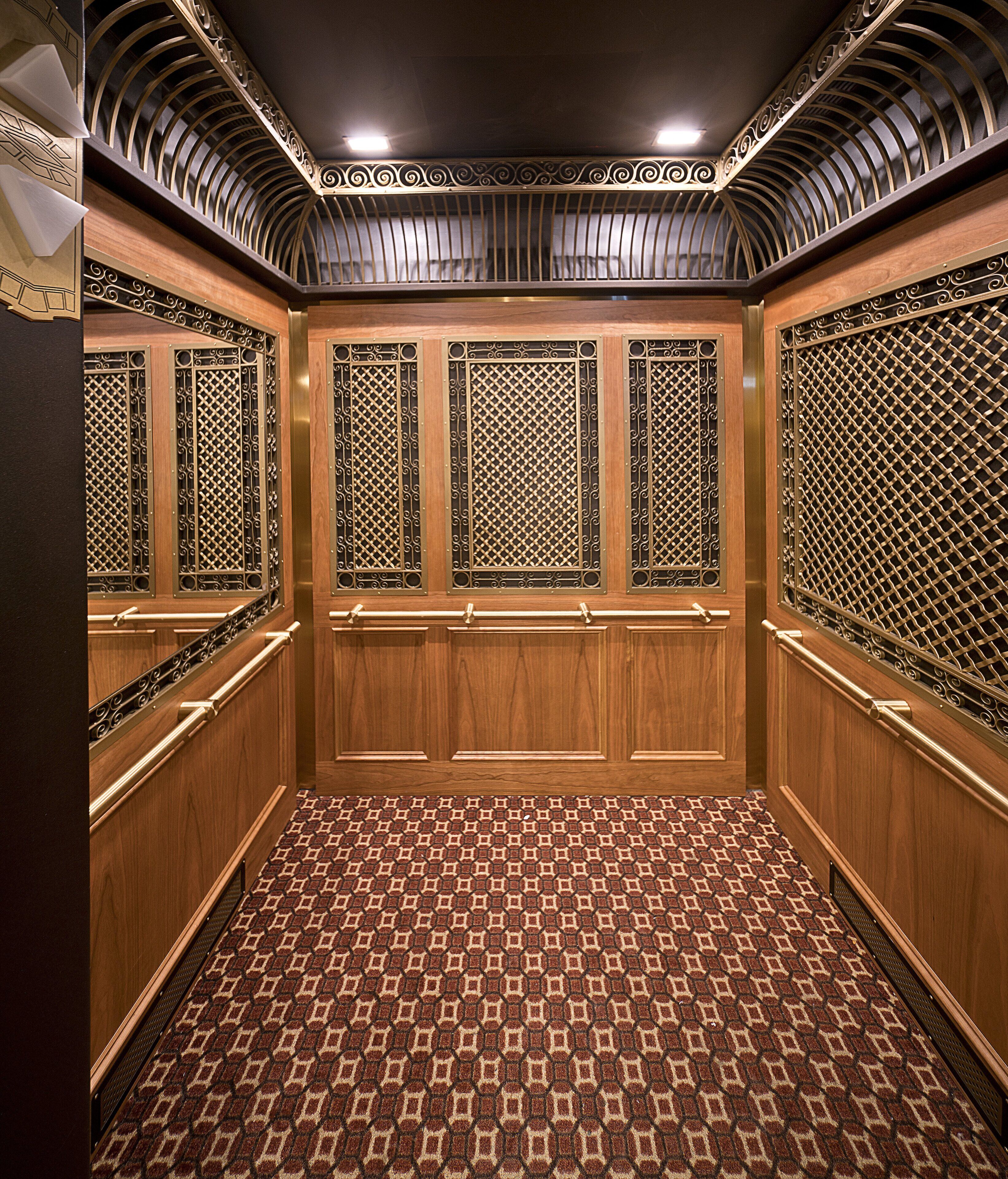 An elevator with wooden walls, metal grills, and a patterned floor.